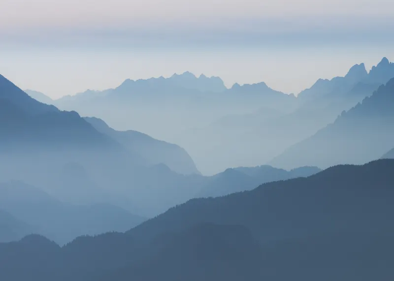 A landscape photograph showing multiple layers of blue mountains fading into the distance through a soft haze.