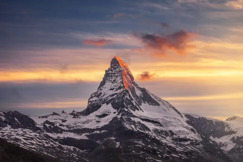 The Matterhorn at sunrise, its east face illuminated by golden light, set against a colorful sky.