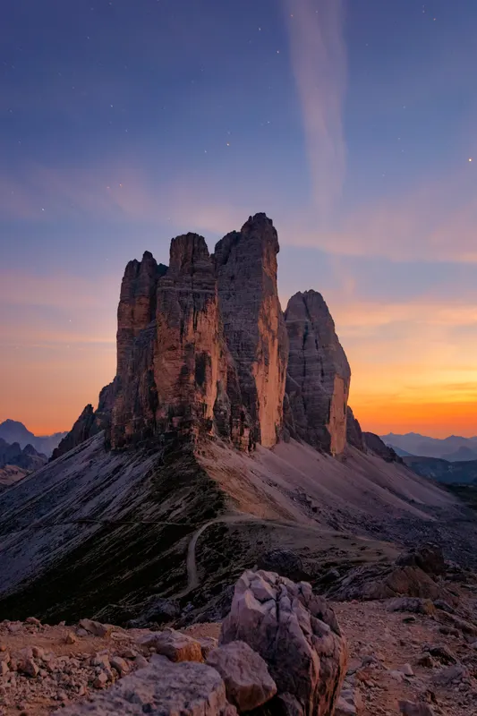 The Three Peaks in the Dolomites at sunset, with an orange horizon and a starry twilight sky above the rocks.
